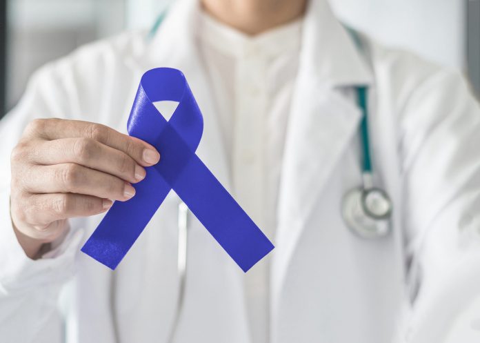 Dark blue ribbon for colon - colorectal cancer awareness on medical doctor's hand support
